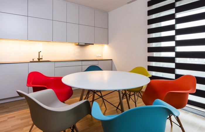Bílo šedá kuchyň s kulatým jídelním stolem a barevnými židličkami
